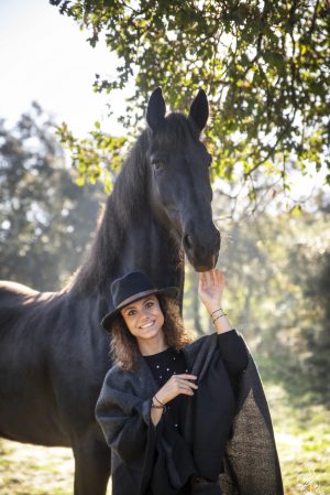 Cheval noir frison au lever du soleil avec une jeune femme devant lui qui lui touche le museau
